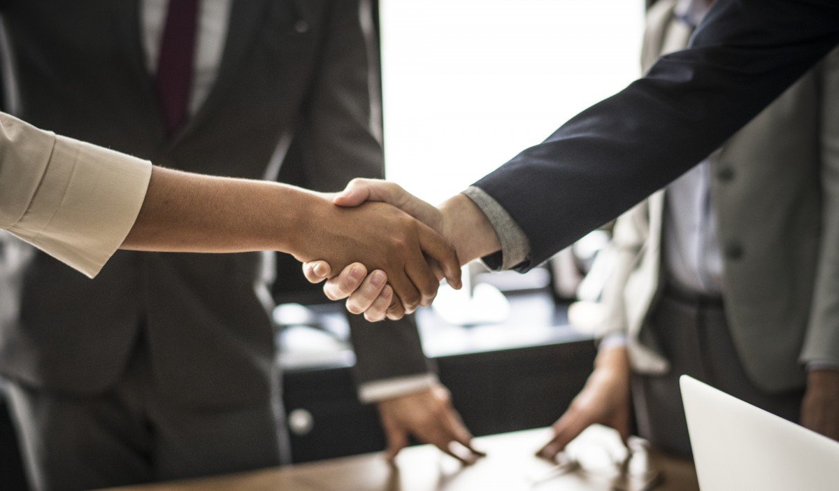 Two people shaking hands across a business meeting table; illustrative stock photograph.